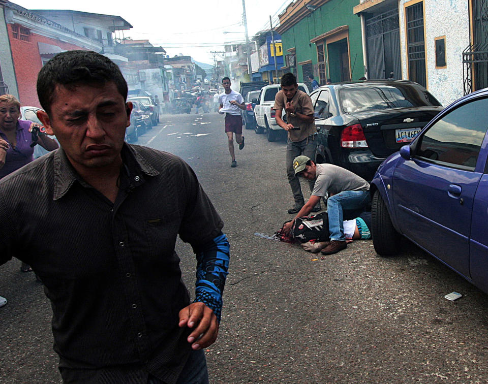 Un hombre asiste a un joven herido durante una protesta contra el gobierno de Nicolás Maduro en San Cristóbal, Venezuela, el martes 24 de febrero de 2015. El joven de 14 años identificado como Kluiverth Roa, según el concejal de esa localidad José Vicente García, recibió un disparo en la cabeza durante enfrentamientos entre los manifestantes y la policía, que intentaba dispersarlos. Murió camino al hospital. (Foto AP)