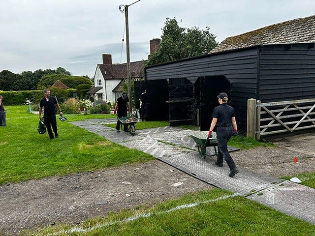 Police with wheelbarrows outside a back barn