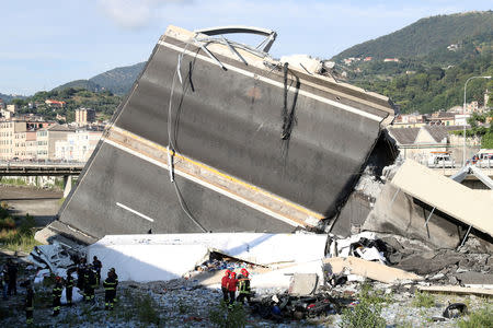 Firefighters and rescue workers stand next to a part of the motorway, at the collapsed Morandi Bridge site in the port city of Genoa, Italy August 14, 2018. REUTERS/Stefano Rellandini