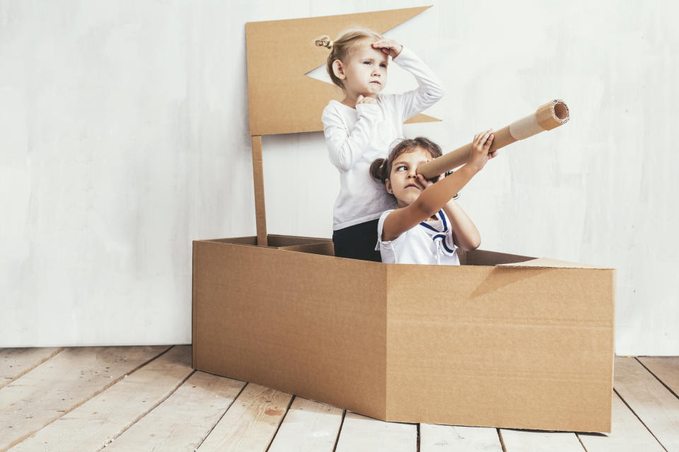 Two children little girls home in a cardboard ship play captains and sailors