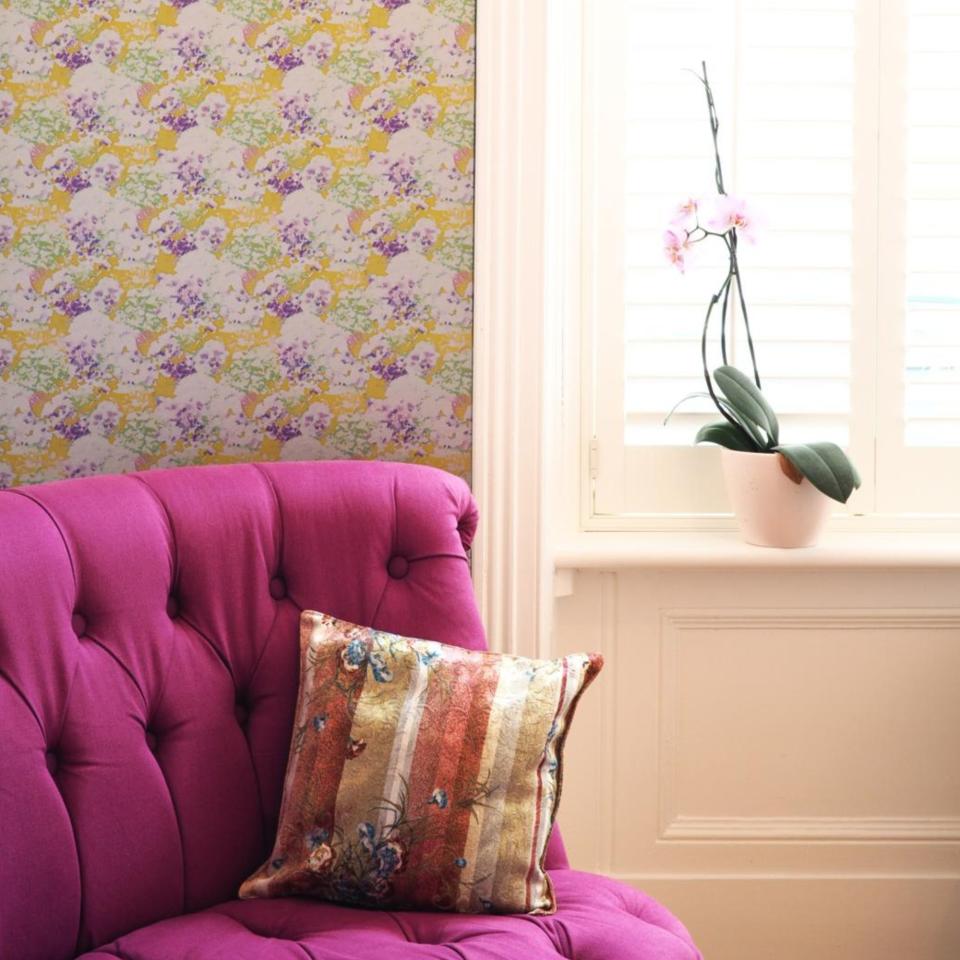 A hot pink armchair beside a clear side table and orchid, decluttered in the French style