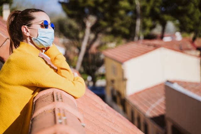 young woman at home on a terrace wearing protective mask and enjoying a sunny day. Corona virus Covid-19 concept