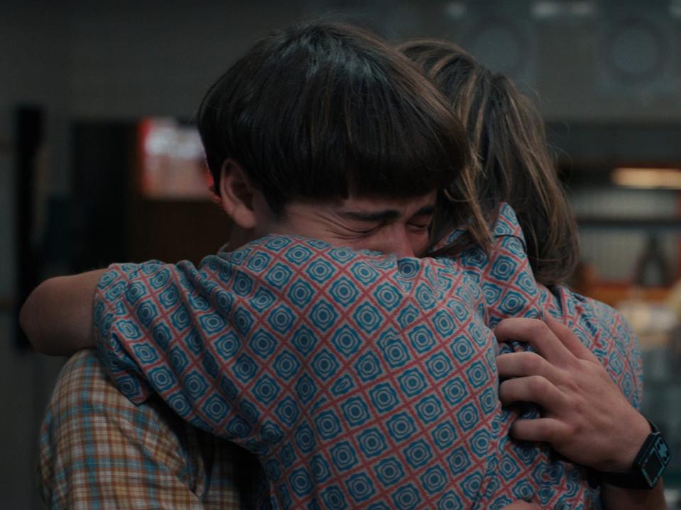 Two teenage boys with brown hair (Will and Jonathan Byers) embrace each other.