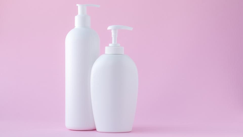 A set of white shampoo and conditioner bottles against a pink background