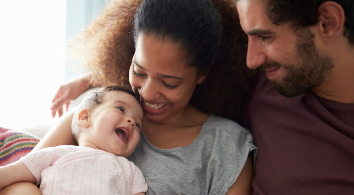 Two smiling parents hold a smiling baby while sitting down.