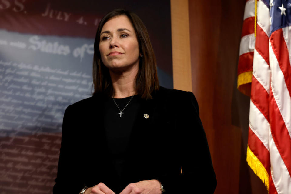 A woman in a black suit with a cross hung around her neck