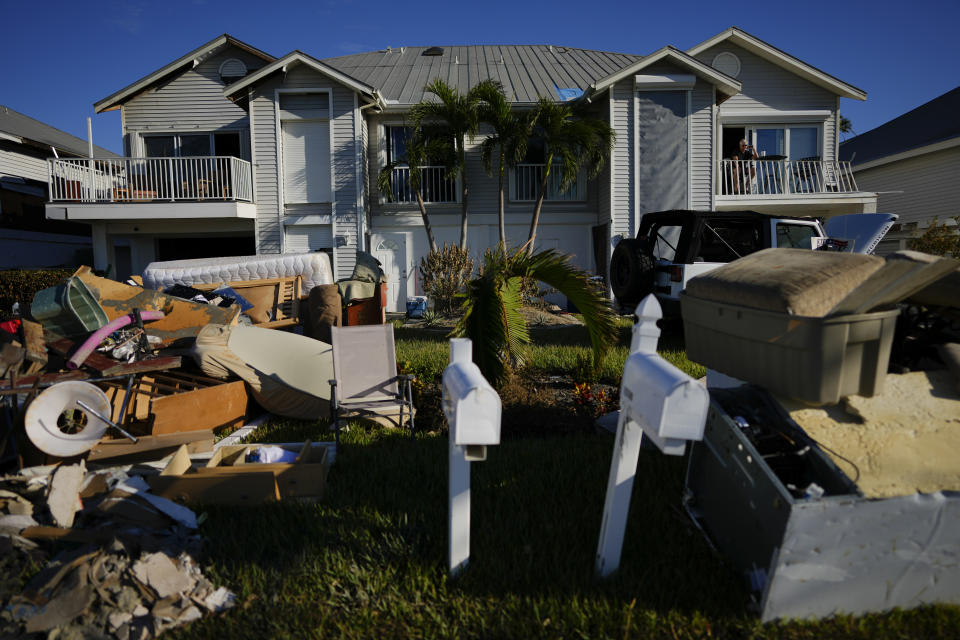 Darryl Hudson of Ontario, Canada, has a morning coffee on the damaged balcony of his vacation home, as water-damaged furniture, debris, and vehicles sit on the lawn after storm surge filled the first story of his and surrounding homes during the passage of Hurricane Ian, near San Carlos Boulevard in Fort Myers Beach, Fla., Sunday, Oct. 2, 2022. (AP Photo/Rebecca Blackwell)