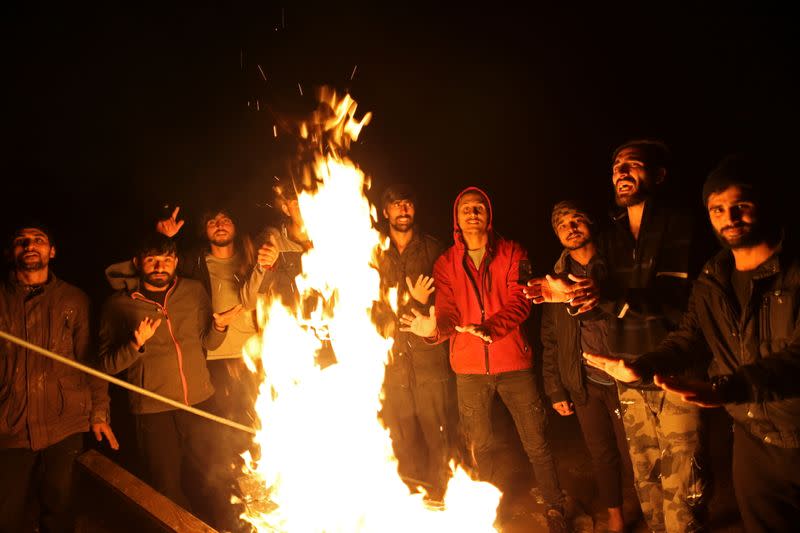 Migrants warm up around a fire at camp "Lipa" after it was closed, in Bihac