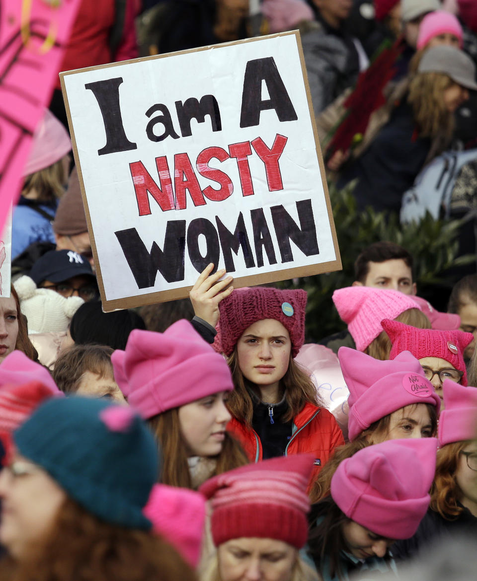 ARCHIVO - Una mujer con un letrero en medio de una ola de gorros rosados antes de la marcha de las mujeres con más de 100.000 participantes el 21 de enero de 2017, en Seattle. Las mujeres marcharon en solidaridad con la Marcha de las Mujeres en Washington para apoyar las causas de las mujeres. La influencia simbiótica del color rosado, con el impulso de una fuerza cultural, fue evidente en 2017 en la Marcha de las Mujeres en Washington, donde las manifestantes se pusieron "gorros de gatito" de color rosa vibrante. (Foto AP/Elaine Thompson, archivo)