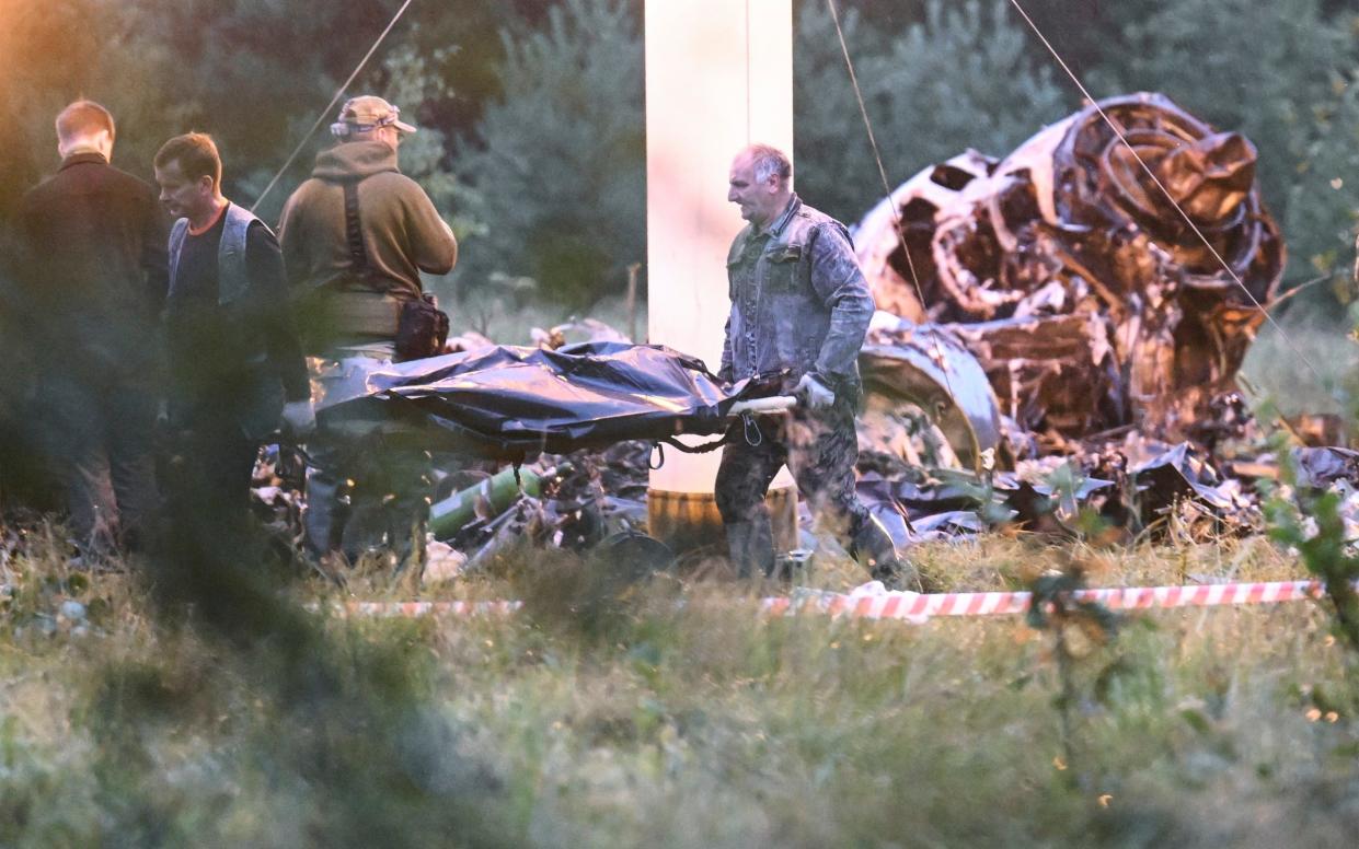 People carry a body bag away from the wreckage of a crashed private jet, near the village of Kuzhenkino, Tver region, Russia
