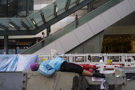 A protester of the Occupy Central movement, blocking the main road leading to the financial Central district in Hong Kong, sleeps on a divider as people travel onto a footbridge October 7, 2014. REUTERS/Tyrone Siu