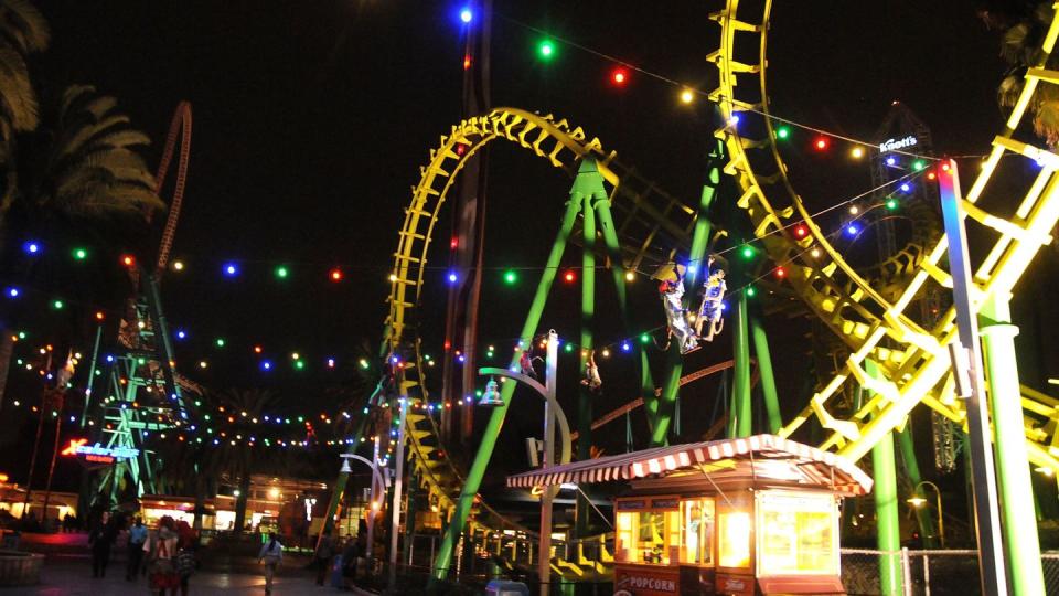 roller coaster, popcorn stand, and other rides lit up at night at knott's scary farm halloween festival in california