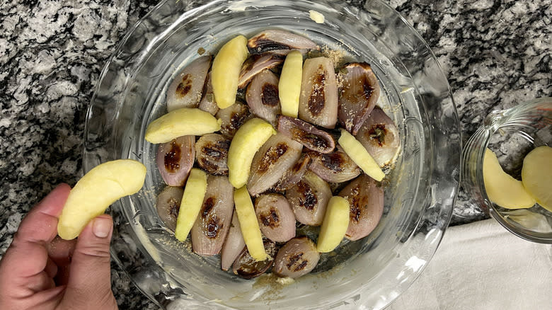 hand adding apples to shallots in pie pan