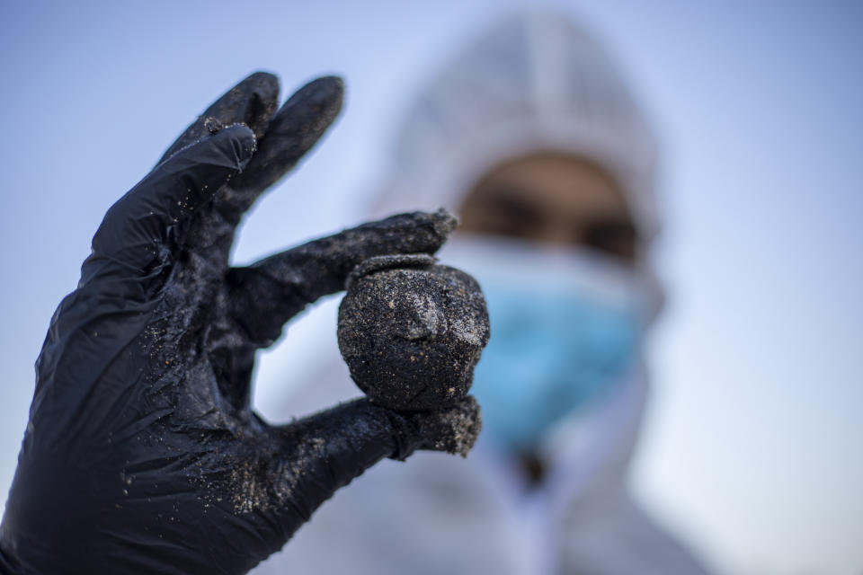 An Israeli soldier wearing a full protective suit holds a piece of tar from an oil spill in the Mediterranean Sea during a cleanup operation at Sharon Beach Nature Reserve, near Gaash, Israel, Monday, Feb. 22, 2021. (AP Photo/Ariel Schalit)