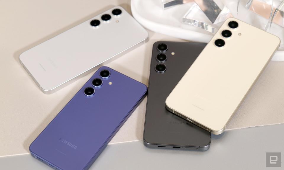 چهار گوشی گلکسی اس 24 در رنگ‌های سفید، کرم، مشکی و بنفش روی میز قرار گرفته‌اند و دوربین‌های عقب آن‌ها رو به بالا است.