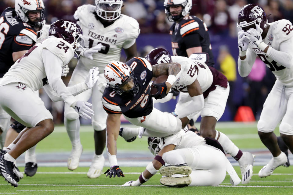 Oklahoma State running back Ollie Gordon II (0) dives for extra yardage past Texas A&M defensive backs Bryce Anderson, bottom right, and Dalton Brooks (25) during the second half of the Texas Bowl NCAA college football game Wednesday, Dec. 27, 2023, in Houston. (AP Photo/Michael Wyke)