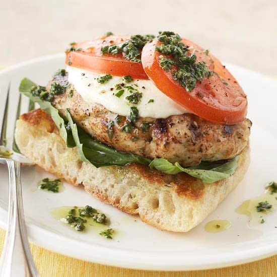 Fresh mozzarella cheese tops these grilled chicken burgers. They're served on a slice of ciabatta bread that's been topped with fresh basil leaves.