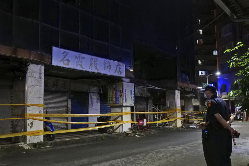 A security person stands across the street from a burnt building in Kaohsiung in southern Taiwan, Thursday, Oct. 14, 2021. Officials say at least 46 people were killed and over 40 injured after a fire broke out in a decades-old mixed commercial and residential building in the Taiwanese port city of Kaohsiunging. Neighborhood residents say the 13-story building was home to many poor, elderly and disabled people and it wasn’t clear how many of the 120 units were occupied. (AP Photo/Huizhong Wu)