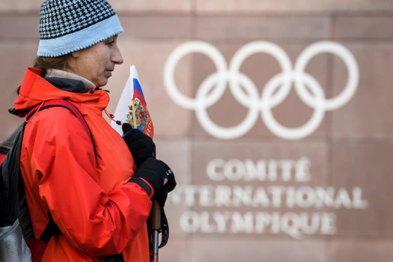 A supporter stands with a Russian flag in front of the logo of the International Olympic Committee headquarters