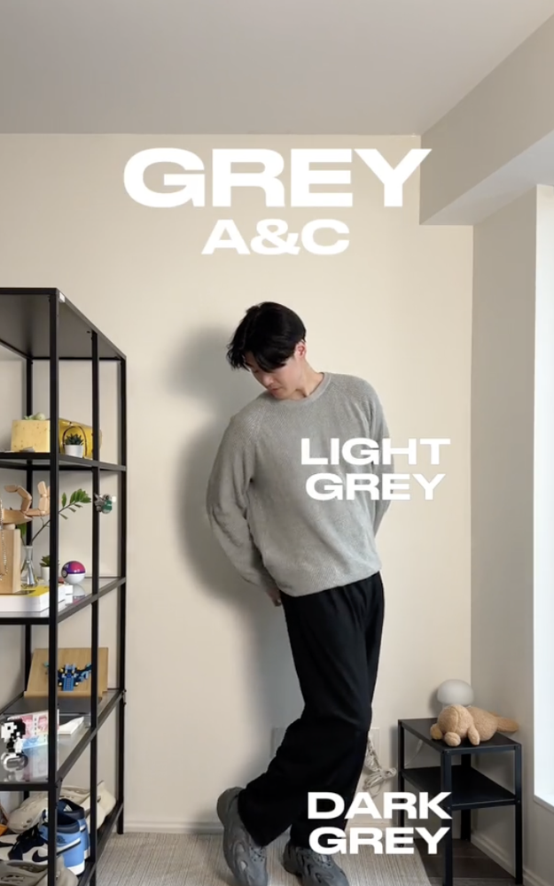 Person in oversized grey sweater and dark pants standing in room, text labels different shades of grey on clothing and decor