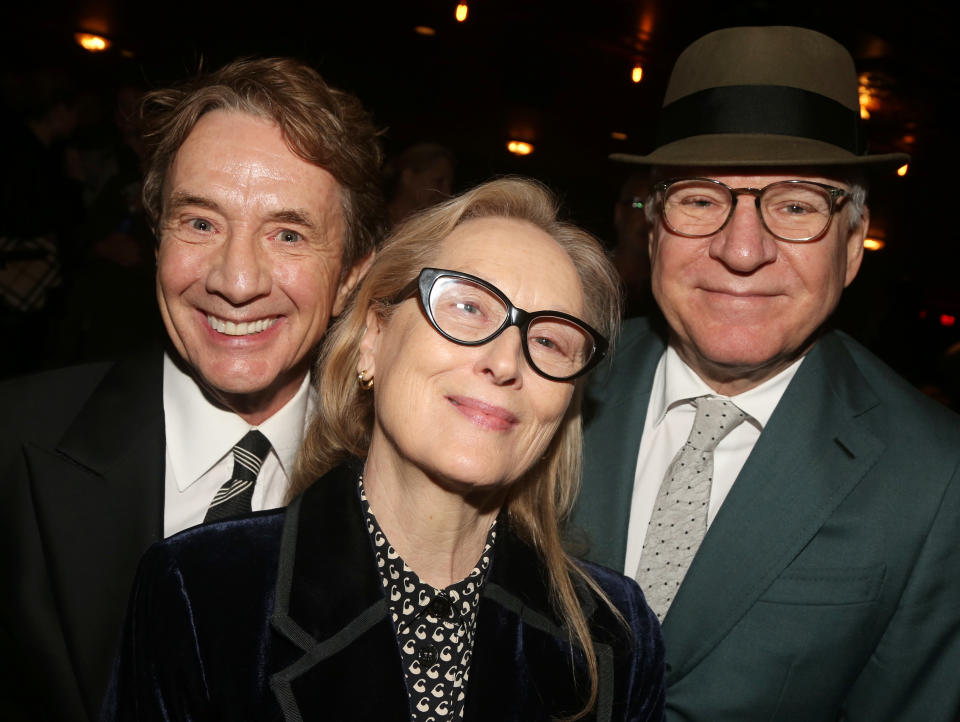 Three smiling celebrities in formal attire at an event