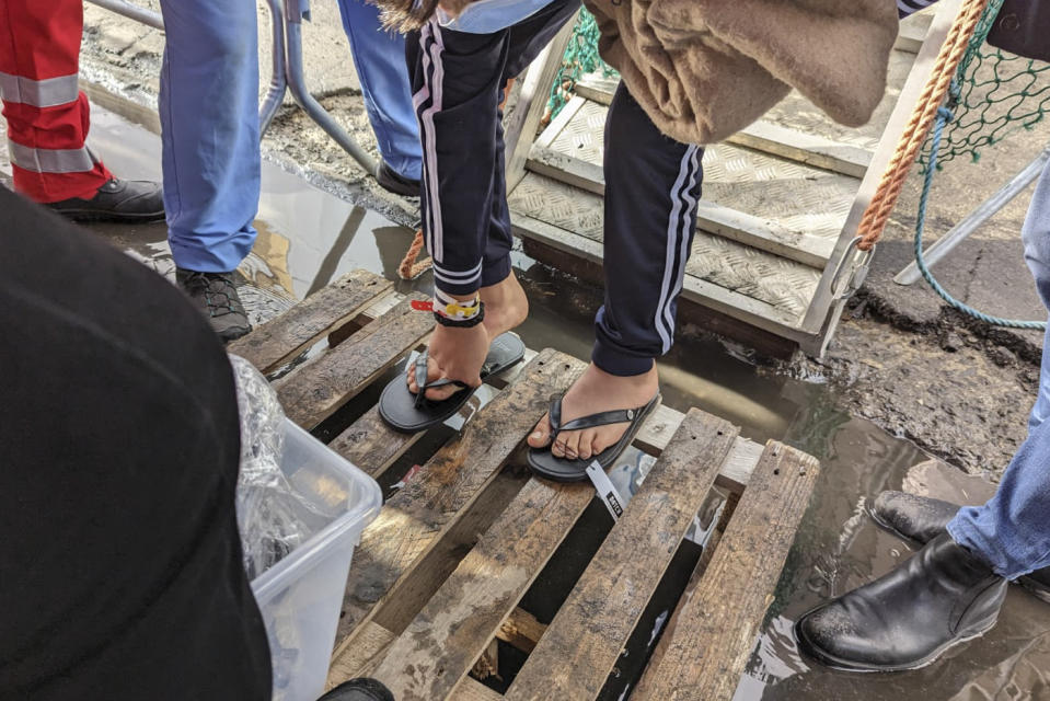 Plastic slippers are given to a man disembarking from the Geo Barents rescue ship carrying on board rescued migrants in the mediterranean sea and docked at the Salerno harbor, Italy, Sunday, Dec. 11, 2022. (MSF Via AP)