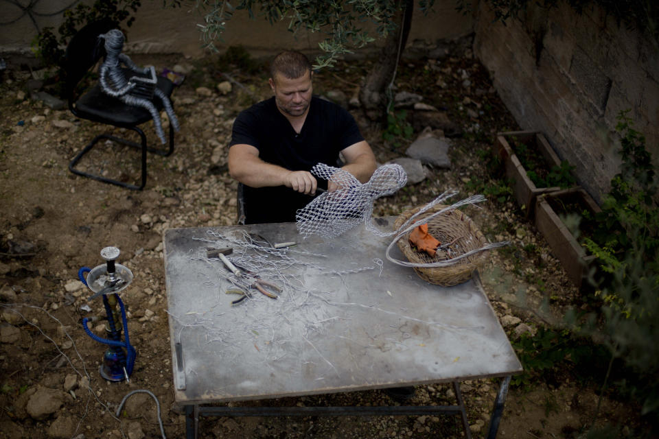 In this Saturday, Nov. 2, 2019 photo, Palestinian artist Haitham Khateeb, uses old metal wire to make art objects reflecting scenes of Palestinian daily life, in the garden of his small house, in the West Bank village of Bilin near Ramallah. After 14 years as a photographer in the Israeli-occupied West Bank, Khateeb has found his second calling through sculpture, telling stories by recycling metal wire into art. He says that while the effect of a news photo can be fleeting, a work of art remains over time. (AP Photo/Majdi Mohammed)