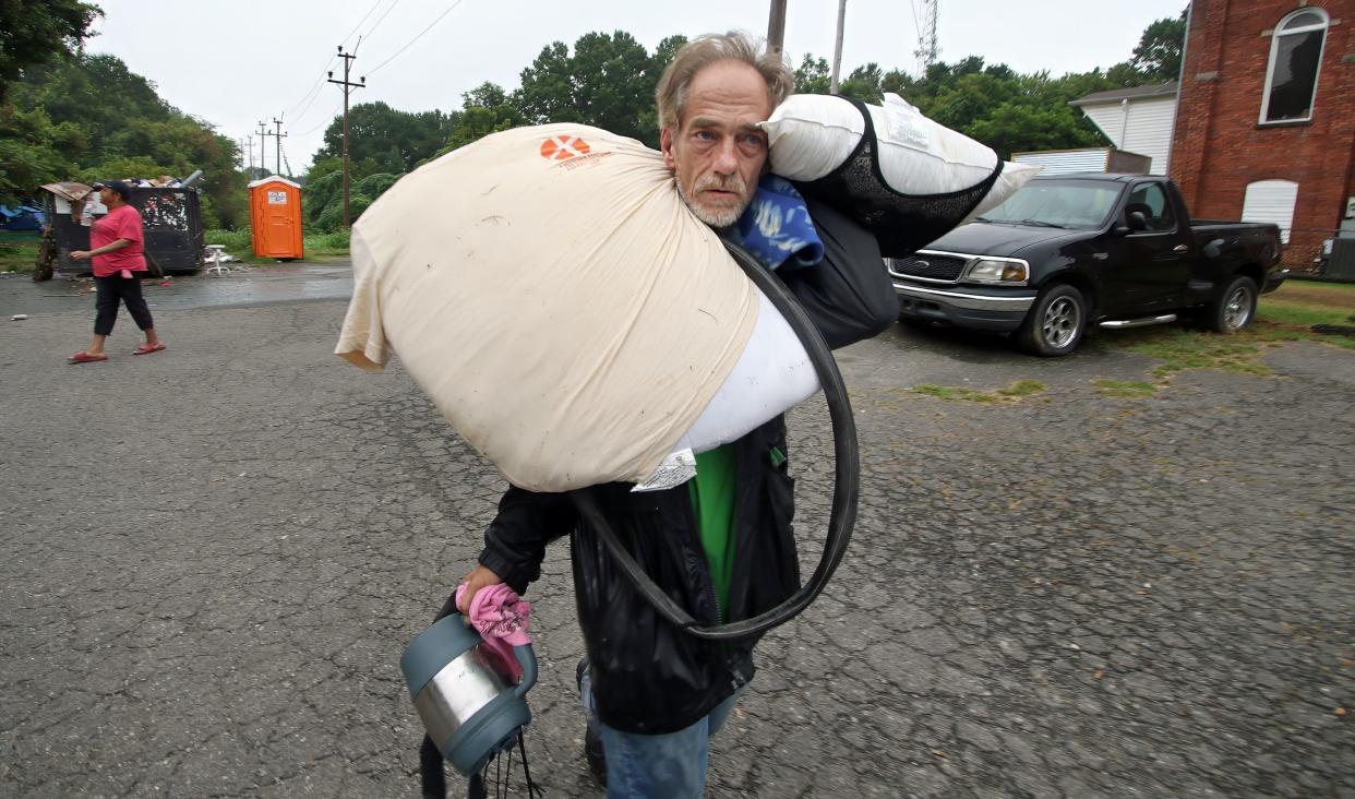 Alfred Gibson carries his belongings away from the homeless encampment behind Faith, Hope and Love Community Enrichment Ministries on North Oakland Street early Monday morning.