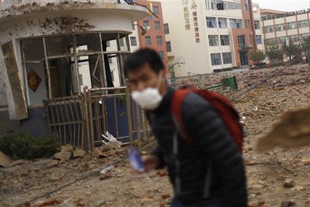 A man wears a mask while walking past a debris-covered basketball court of a school a day after an explosion at a Sinopec Corp oil pipeline in Huangdao, Qingdao, Shandong Province November 23, 2013. REUTERS/Aly Song