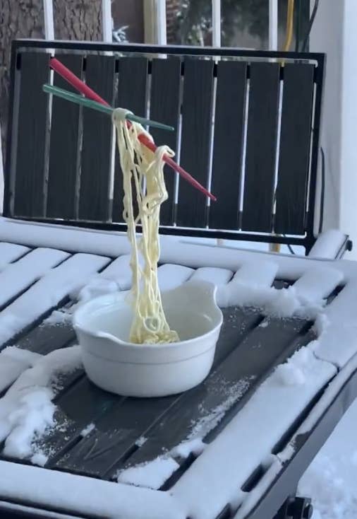 chopsticks and noodles frozen in the air above a bowl