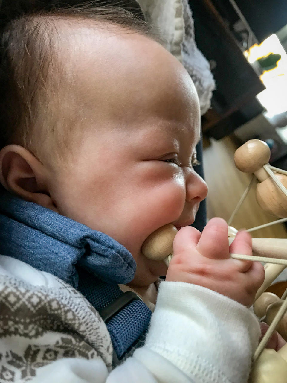 A baby in a patterned outfit is chewing on a wooden toy while seated