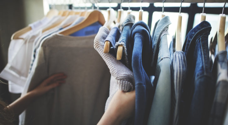 A photo of someone looking at clothing on hangers, hanging from a rack.