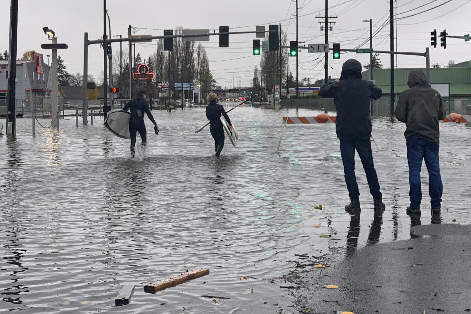 IDENTIFIES CAYLON COOMES AS BEING SECOND FROM LEFT INSTEAD OF AT LEFT - Caylon Coomes, second from left, and another man prepare to paddleboard in floodwaters on city streets in Bellingham, Wash., Monday, Nov. 15, 2021. Widespread flooding in the Pacific Northwest amid days of heavy rainfall caused people to evacuate their homes, stranded drivers, and closed businesses, roads and schools. (AP Photo/Lisa Baumann)