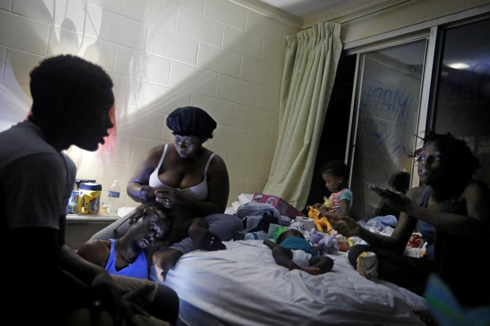 FILE - In this Oct. 16, 2018 file photo, Gabrielle Morgan, center rear, braids the hair of her husband Santional as they sit by a lantern with their children from left, Decoya, 13, Isabella, 3 mos., Gabriella, 3, and Lakevia, 15, in their room at the damaged American Quality Lodge where they continue to live without power in the aftermath of Hurricane Michael in Panama City, Fla. The tropical weather that turned into monster Hurricane Michael began as a relatively humble storm before rapidly blossoming into the most powerful cyclone ever to hit the Florida Panhandle, causing wrenching scenes of widespread destruction. (AP Photo/David Goldman, File