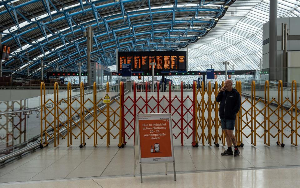 A man talks on his phone next to a barrier blocking access to platforms at Waterloo train station - Carl Court/Getty Images