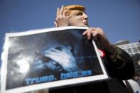 A man holds a photo of Sgt. Elor Azaria and wears the mask of the US President Donald Trump outside the Israeli military court during Azaria's sentencing in Tel Aviv, Israel, Tuesday, Feb. 21, 2017. Azaria was sentenced to 18 months in prison for his deadly shooting of an incapacitated Palestinian attacker in the West Bank city of Hebron, capping a nearly yearlong saga that has deeply divided the country. The sentence, which included one year probation and a demotion in rank, was lighter than expected. Prosecutors had asked for a prison term of three to five years. (AP Photo/Oded Balilty)