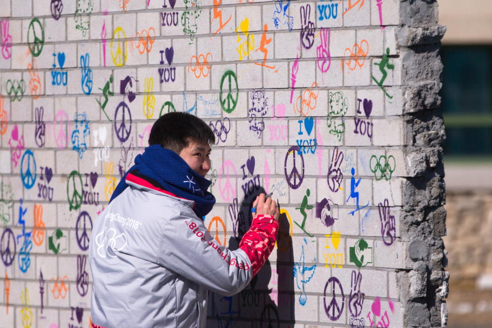 <p>A man writes on the Truce Mural unveiled in the Olympic Village at the 2018 Winter Olympic Games. (Sergei Bobylev\TASS via Getty Images) </p>