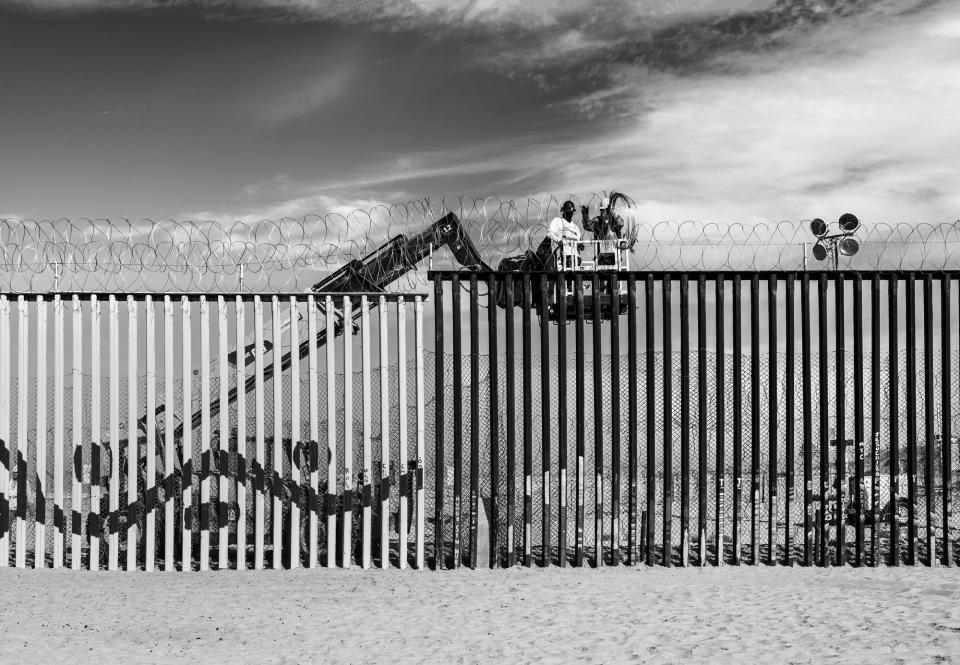 Workers line the top of the border wall with coils of barbed wire in Tijuana, Mexico.