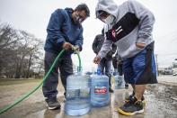 Victor Hernandez, left, and Luis Martinez fill their water containers with a hose from a spigot in Haden Park, Thursday, Feb. 18, 2021 in Houston. Texas officials have ordered 7 million people to boil tap water before drinking it following days of record low temperatures that damaged infrastructure and froze pipes. (Brett Coomer/Houston Chronicle via AP)