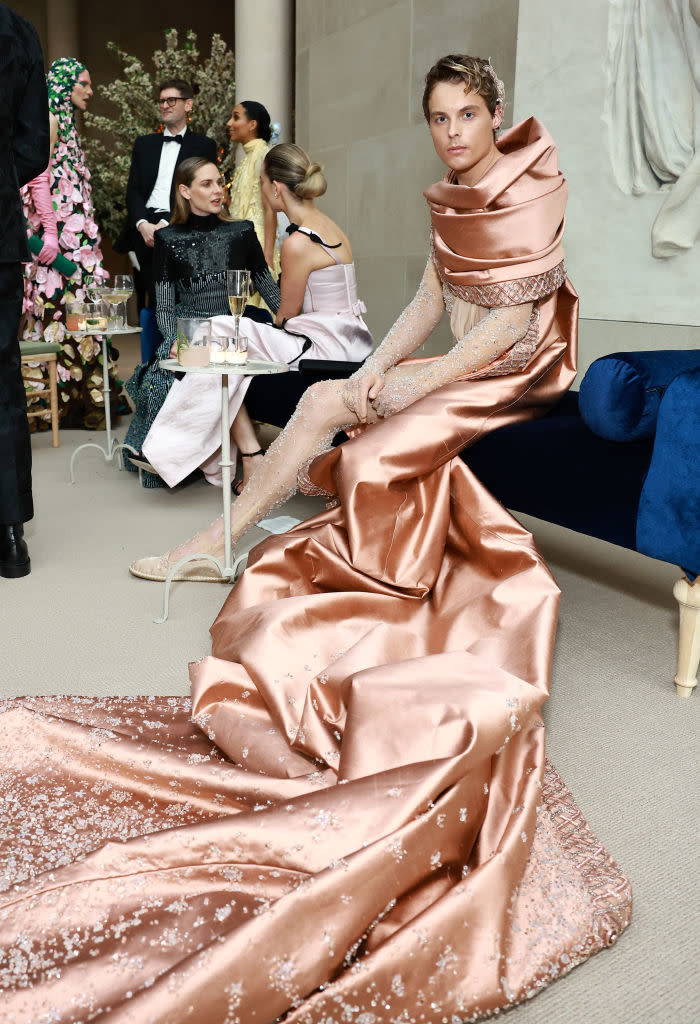 Individual in an elegant, draped satin gown with embellished overlay seated at an event