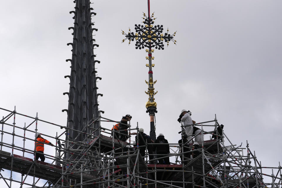 Workers install Notre Dame de Paris cathedral's Croix du Chevet in front of the cathedral spire, left, to be reinstalled Friday, May 24, 2024, in Paris. The Croix du Chevet is the only piece of the cathedral roof that did not burn in the devastating April 2019 fire. (AP Photo/Thibault Camus)