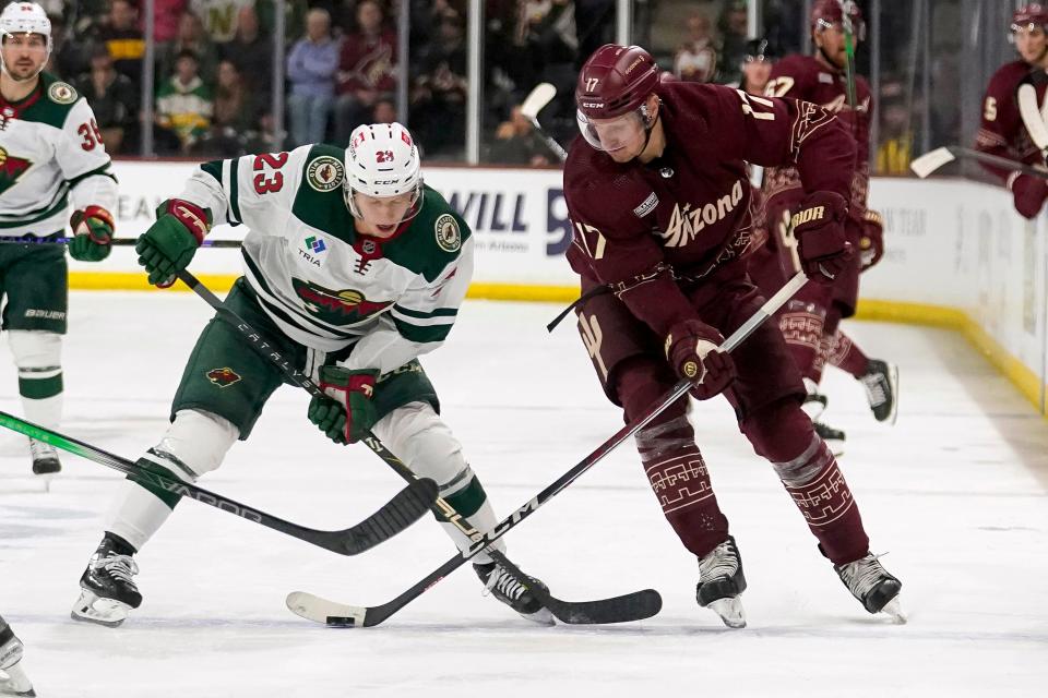 Minnesota Wild's Marco Rossi (23) and Arizona Coyotes' Nick Bjugstad (17) vie for the puck during the third period of an NHL hockey game Wednesday, Feb. 14, 2024, in Tempe, Ariz. (AP Photo/Darryl Webb)