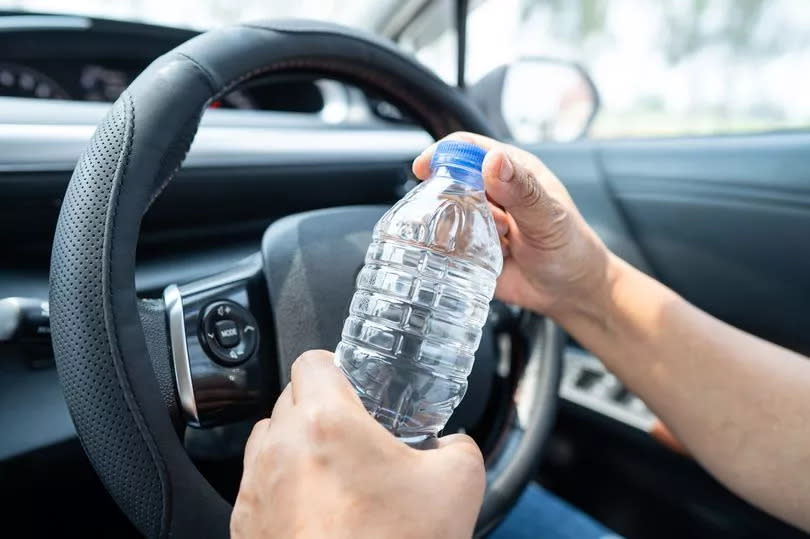 Asian woman driver holding bottle for drink water while driving a car. Plastic hot water bottle cause fire.