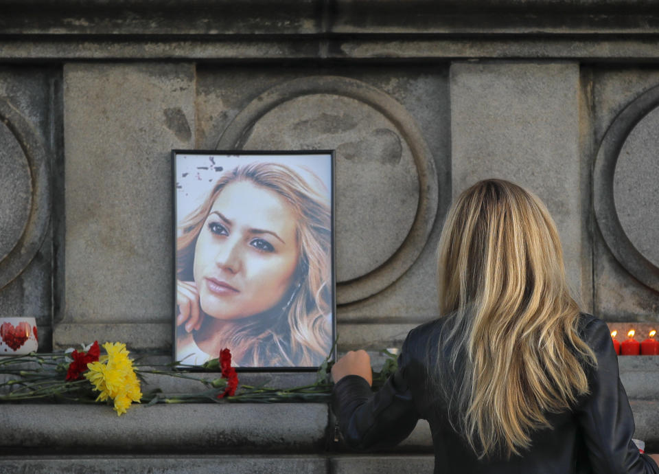 A woman places flowers next to a portrait of slain television reporter Viktoria Marinova during a vigil at the Liberty Monument in Ruse, Bulgaria, Monday, Oct. 8, 2018. Bulgarian police are investigating the rape, beating and slaying of a female television reporter whose body was dumped near the Danube River after she reported on the possible misuse of European Union funds in Bulgaria. (AP Photo/Vadim Ghirda)