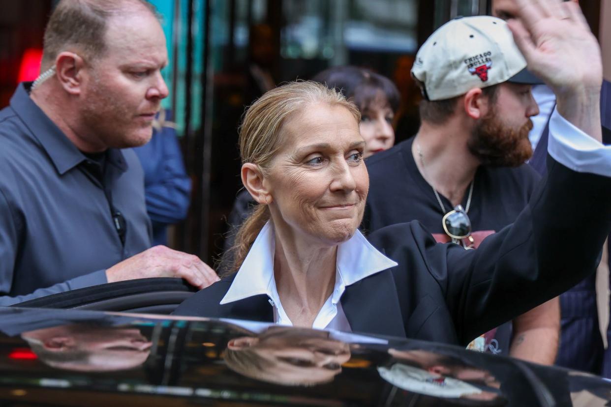 celine dion raises her arm to wave to fans outside a car