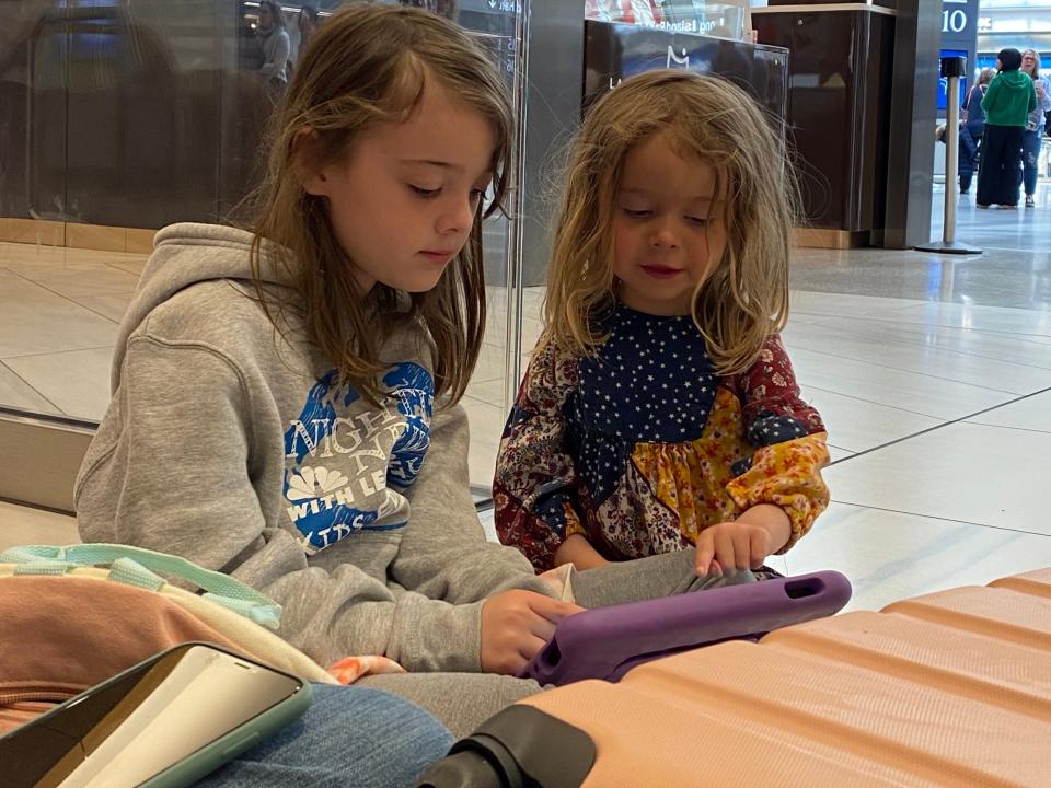 lauren's daughters sitting on the floor of a train station look at a tablet