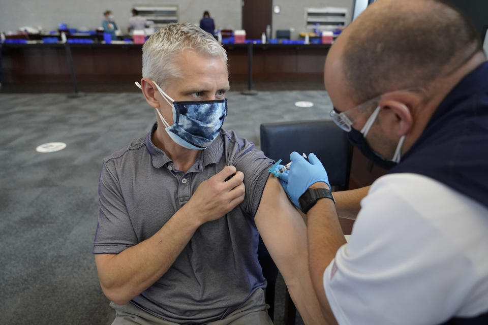 Paul Clasby, of Holliston, Mass., left, receives his second shot of Moderna COVID-19 vaccine from paramedic Jake Lees, of North Attleborough, Mass., right, at a mass vaccination clinic, Wednesday, May 19, 2021, at Gillette Stadium, in Foxborough, Mass. A month after every adult in the U.S. became eligible for the vaccine, a distinct geographic pattern has emerged: The highest vaccination rates are concentrated in the Northeast, while the lowest ones are mostly in the South. (AP Photo/Steven Senne)