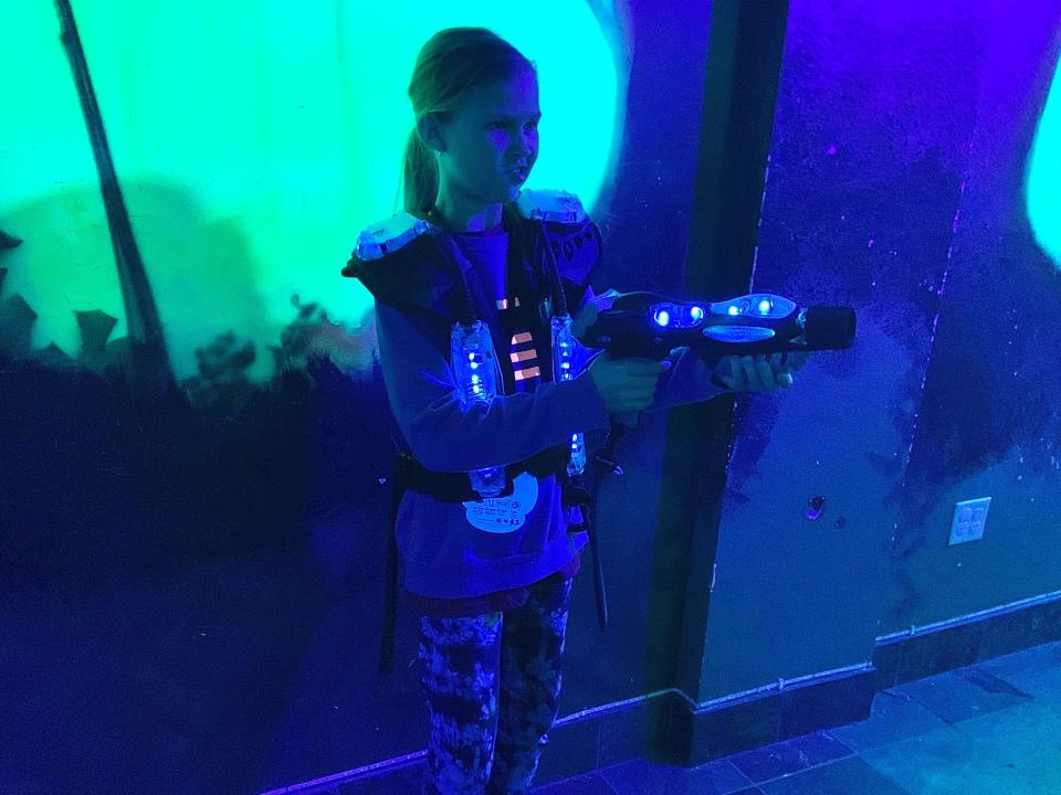 A girl dressed up to play laser tag and pointing her laser gun.