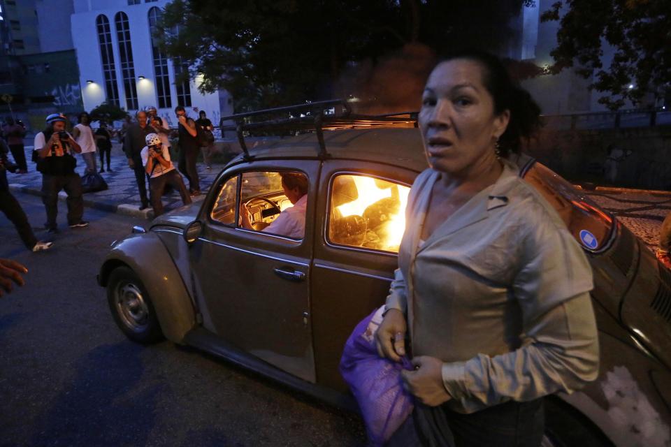 CORRECTS HOW THE CAR CAUGHT FIRE - A man drives his car which caught fire when he tried to drive past a burning barricade set up by protesters who were demanding better public services and protesting against the upcoming World Cup soccer tournament in Sao Paulo, Brazil, Saturday, Jan. 25, 2014. The woman was also in the vehicle but got out when it caught fire. Last year, millions of people took to the streets across Brazil complaining of higher bus fares, poor public services and corruption while the country spends billions on the World Cup, which is scheduled to start in June. (AP Photo/Nelson Antoine)