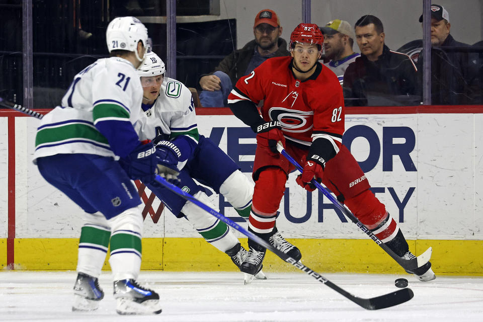 Carolina Hurricanes' Jesperi Kotkaniemi (82) controls the puck between Vancouver Canucks' Sam Lafferty (18) and Nils Hoglander (21) during the third period of an NHL hockey game in Raleigh, N.C., Tuesday, Feb. 6, 2024. (AP Photo/Karl B DeBlaker)